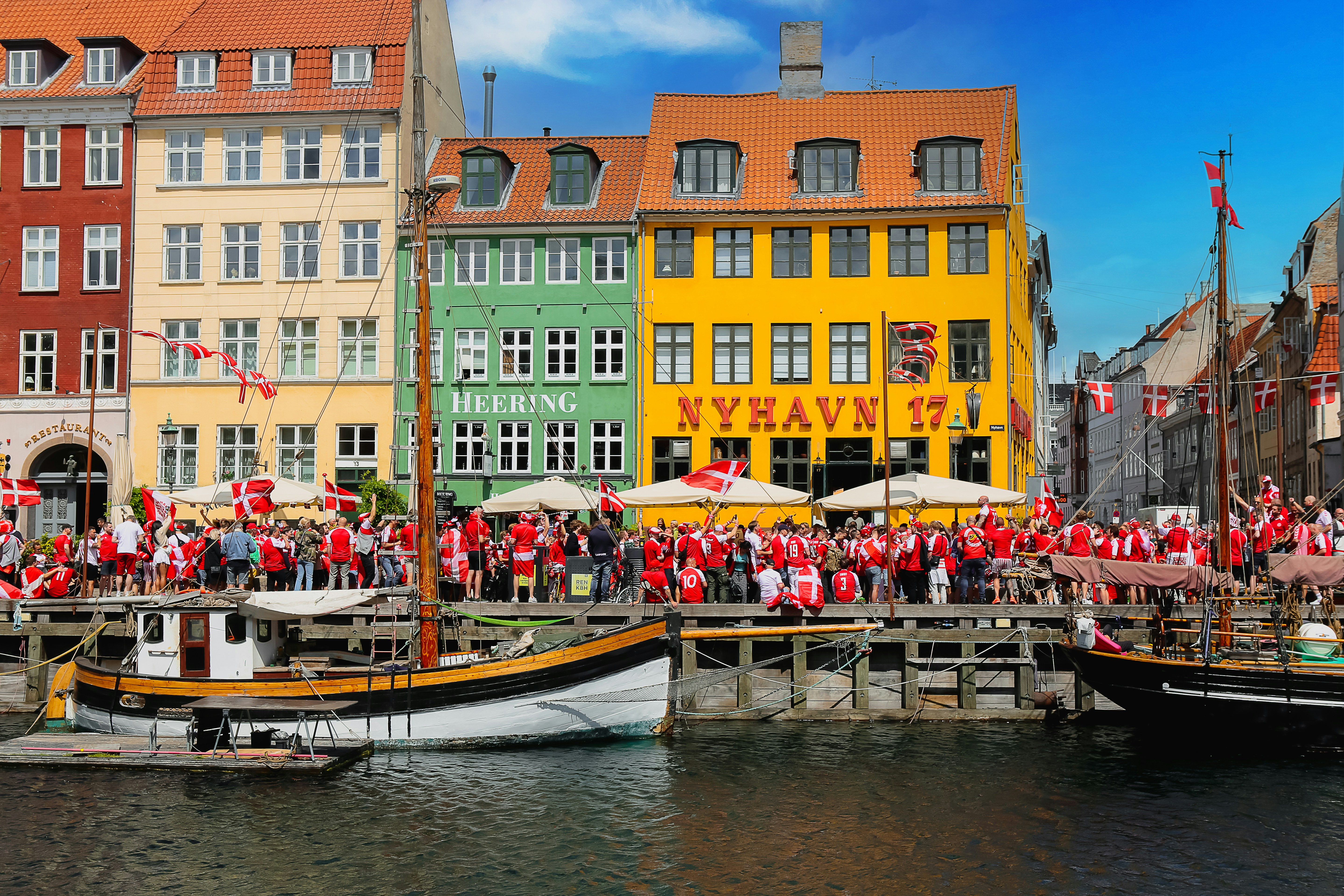 Dänische Fußballfans feiern vor bunten Häusern im Hafen Nyhavn in Kopenhagen