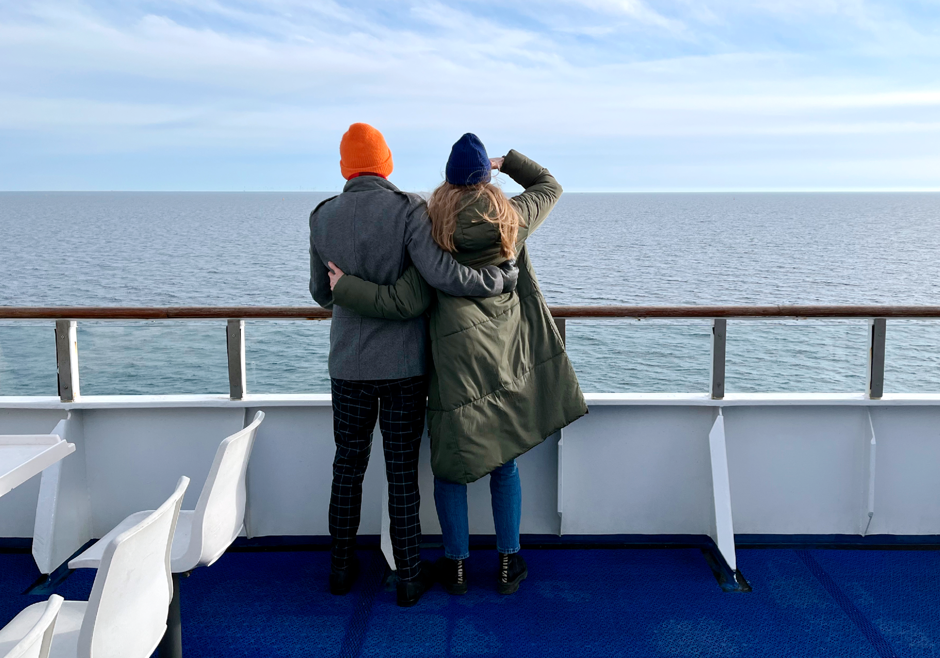 Young couple on the ferry deck in winter coats overlooking the ocean