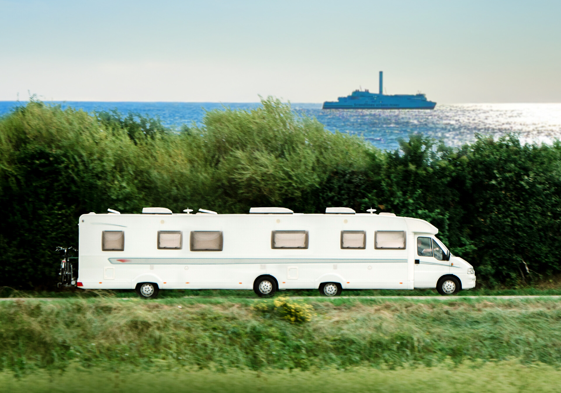 Long autocamper driving next to the ocean where you can see a scandlines ferry