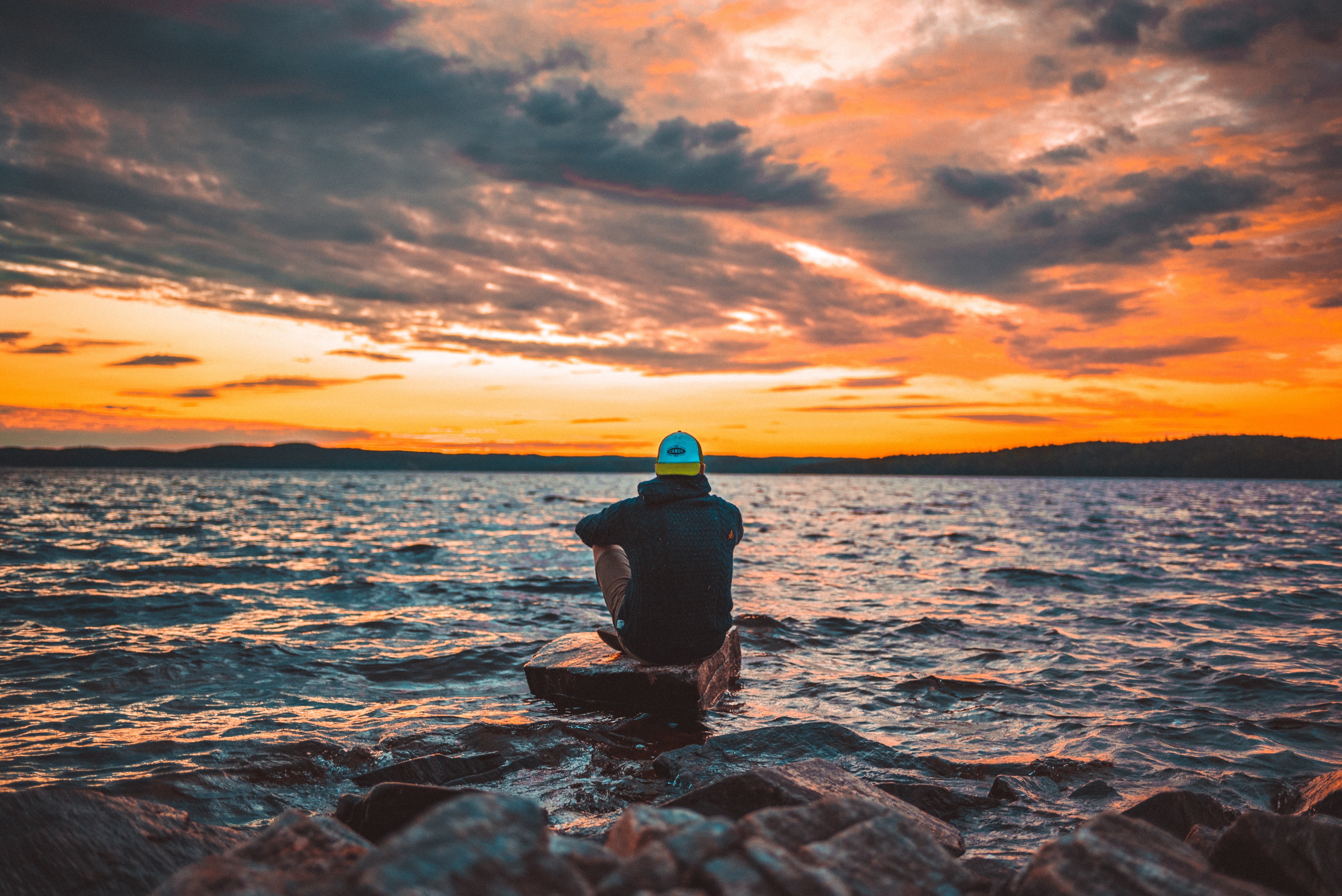 Ein Mensch sitzt auf dem Stein am Wasser und beobachten Sonnenuntergang am Meer