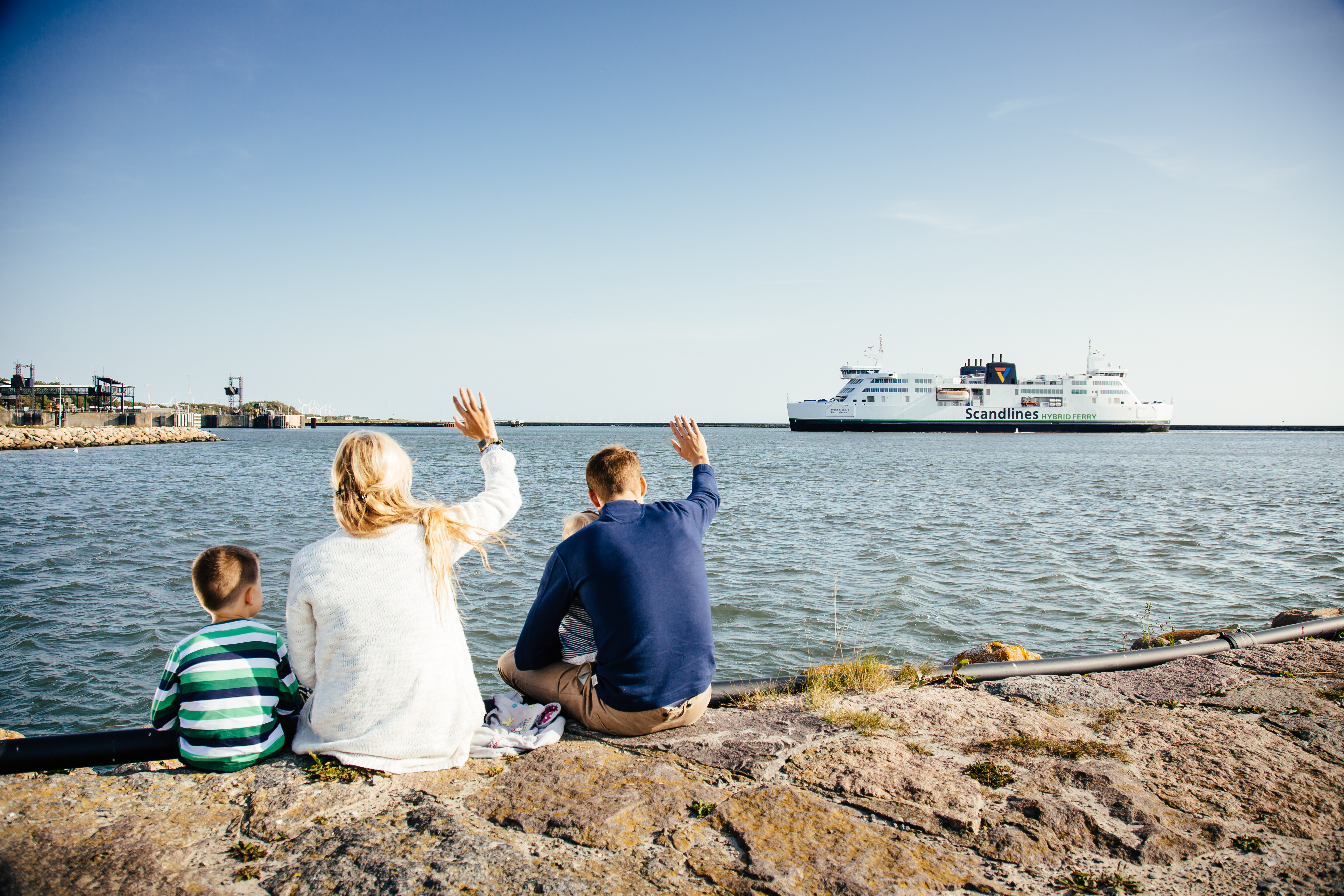 Familie sitzt am Meer und begrüßt anreisende Scandlines hybrid ferry