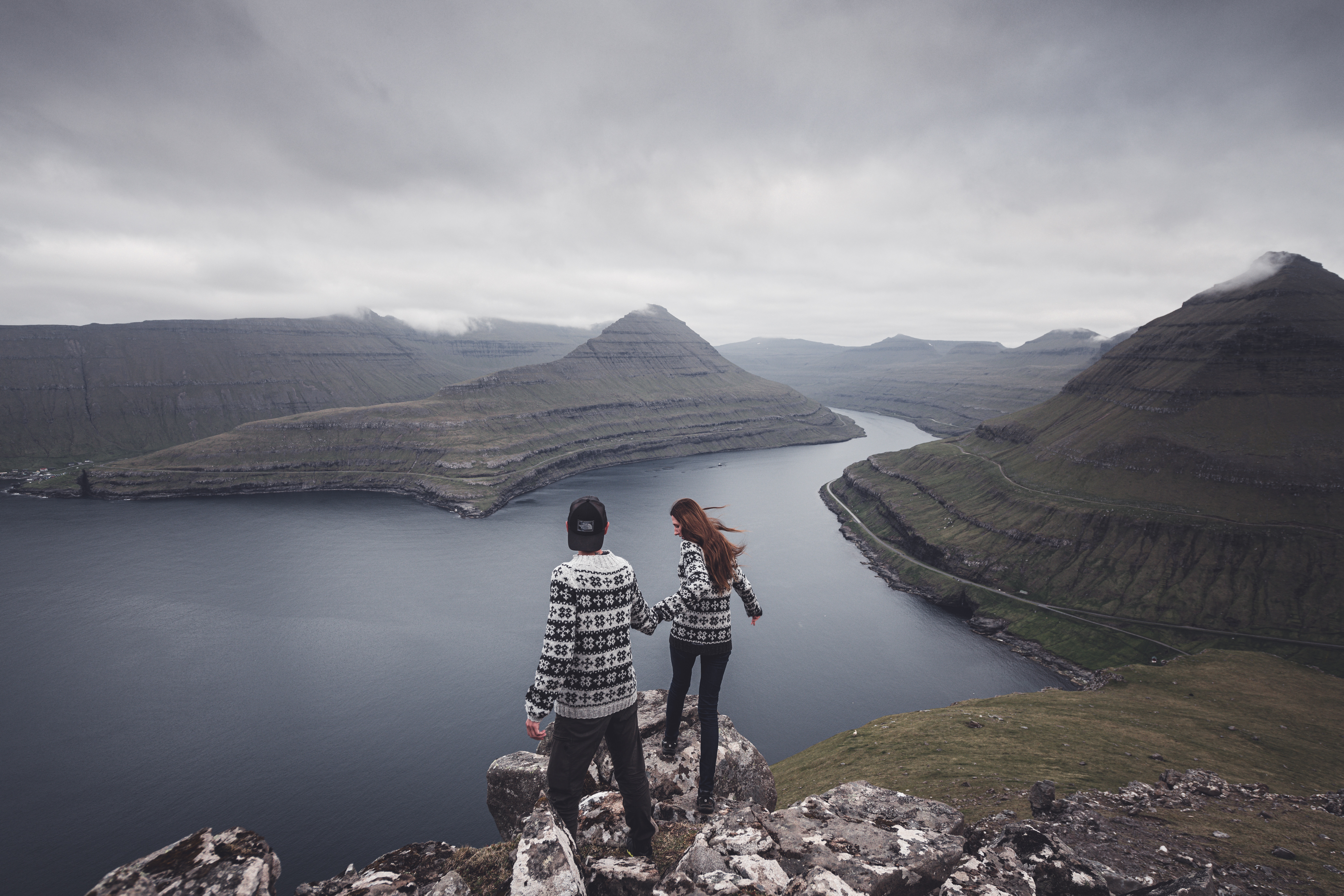 Ein Paar steht an Klippen und beobachtet von oben die skandinavische Berglandschaft am Wasser