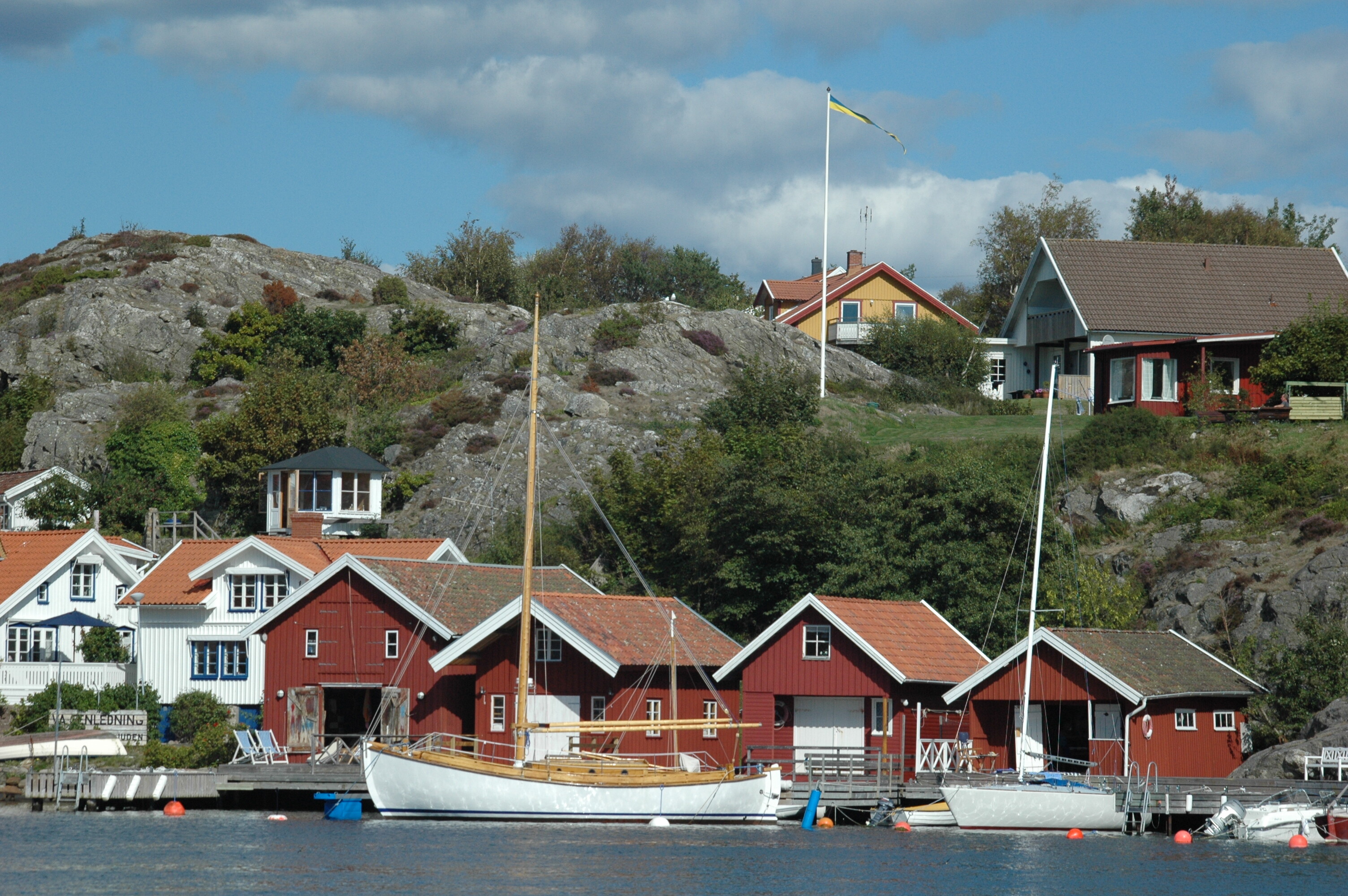 Typische rote Häuser in Schweden am Wasser mit dem Boot und einer schwedischer Flagge