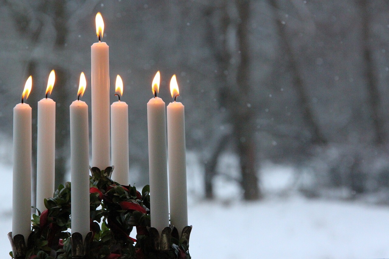 Lange weiße Kerzen leuchten, draußen stehen Bäume im Schnee