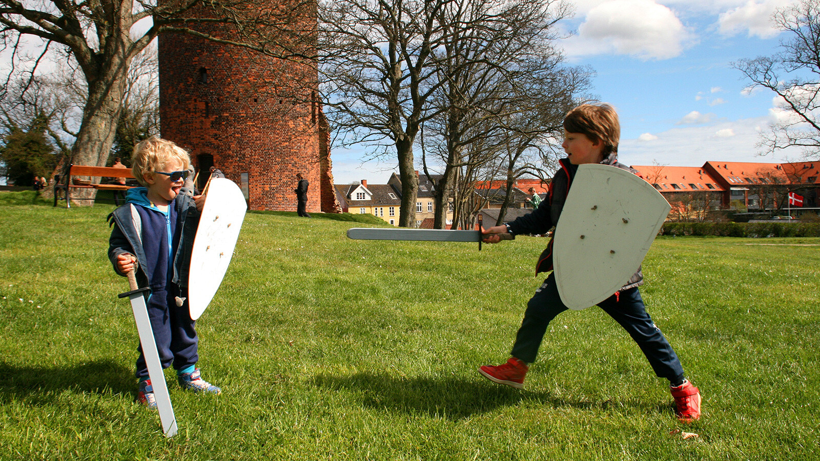 2 kleine Kinder spielen als Ritter auf der Wiese im Burgzentrum Vordingborg