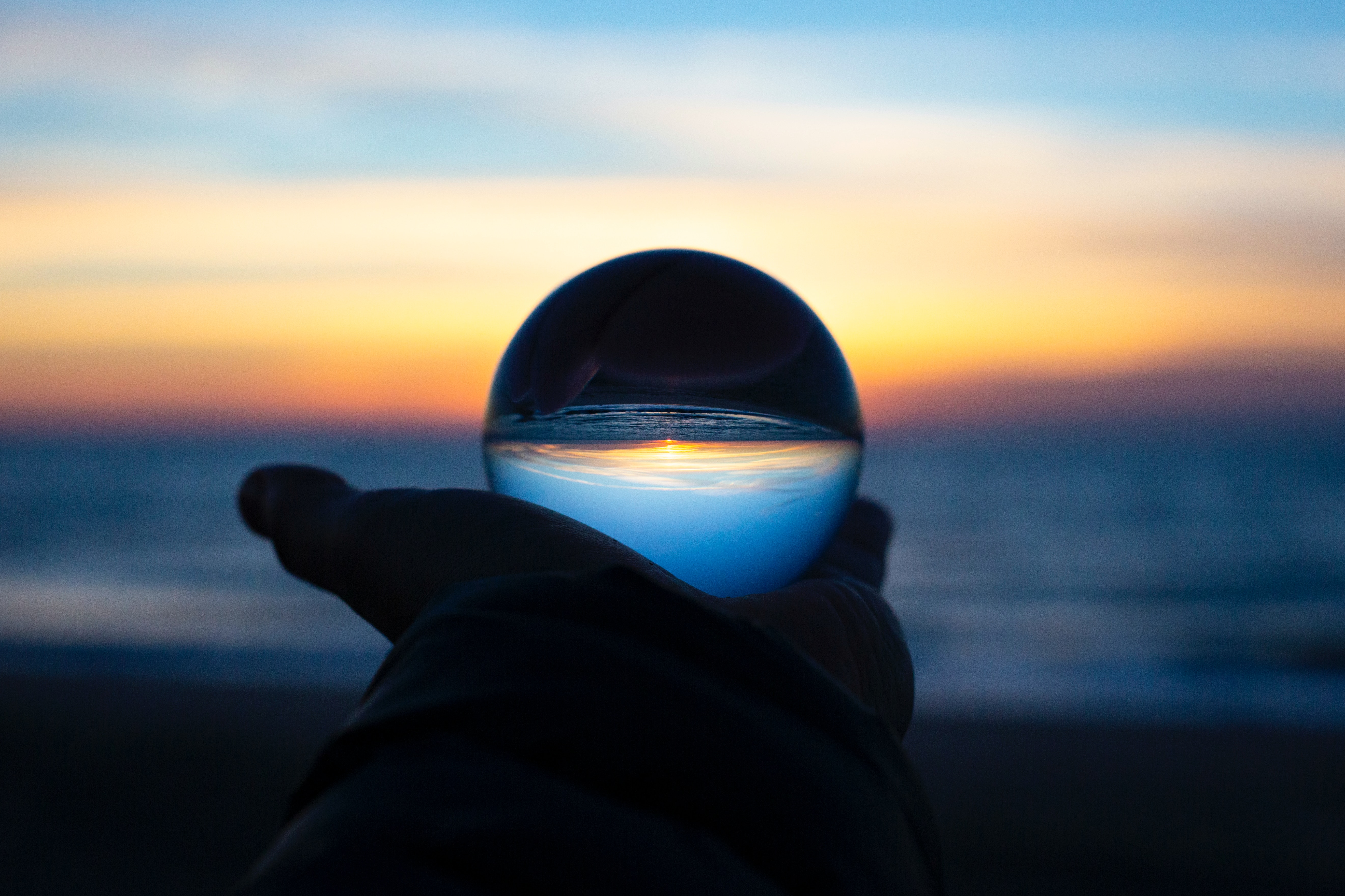 Glaskugel im Hand mit dem Meer beim Sonnenuntergang im Hintergrund