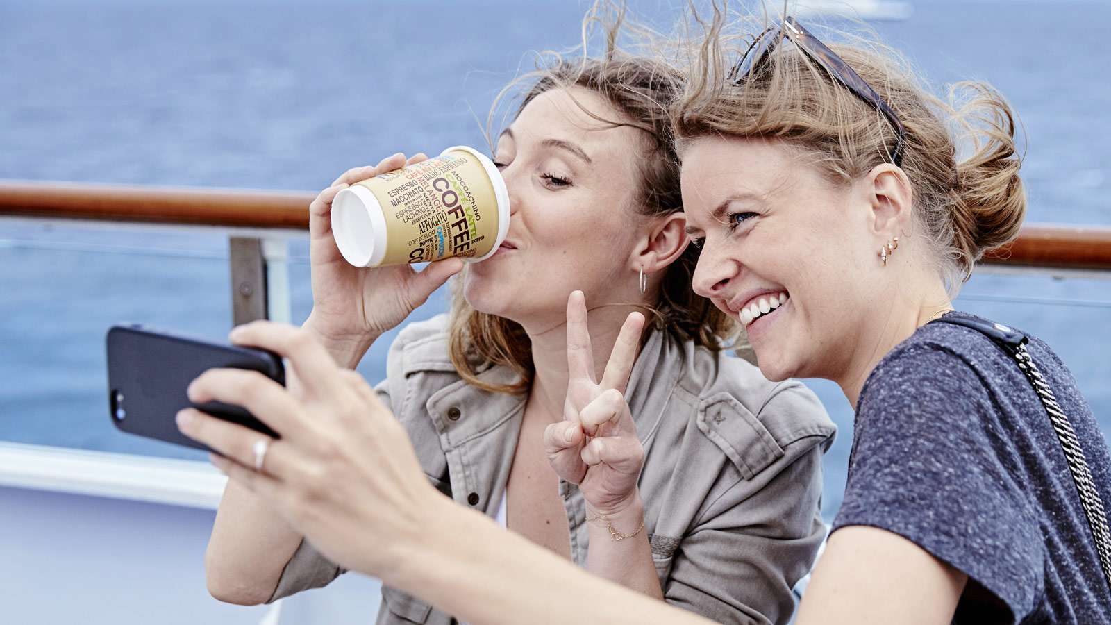 To kvinder på færgens soldæk drikker kaffe og tager selfie
