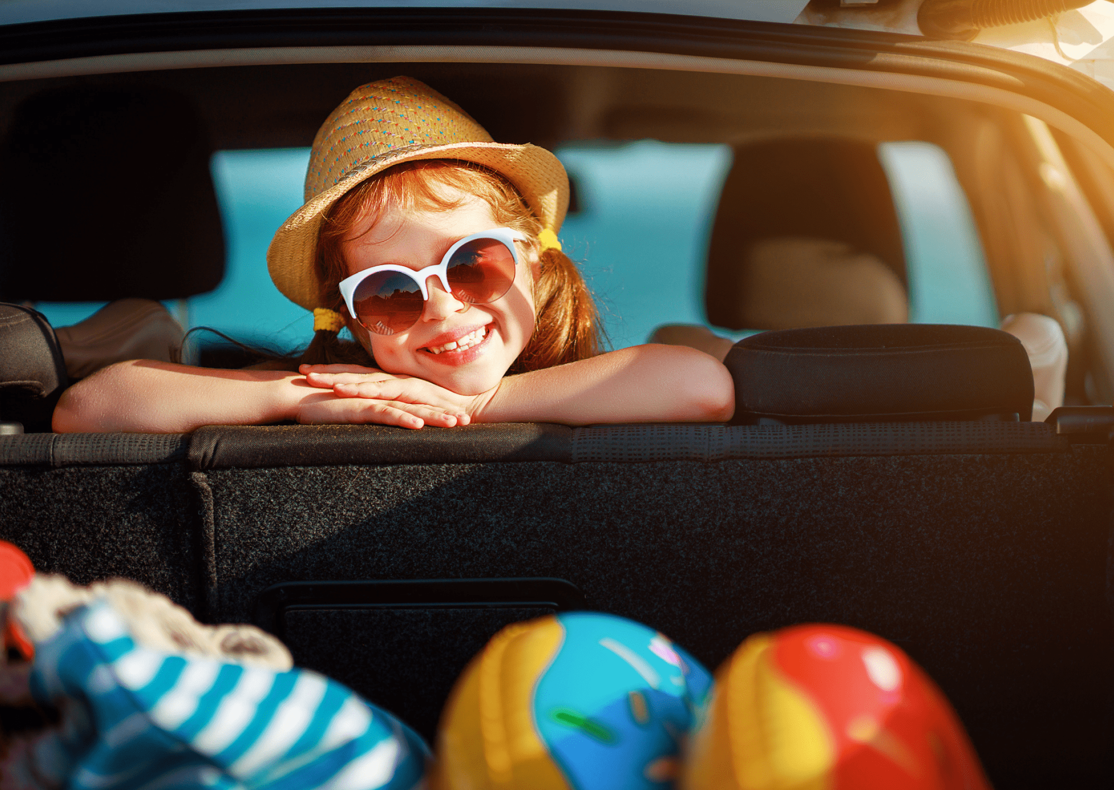 Pige med solbriller smiler ud af bagagerummet