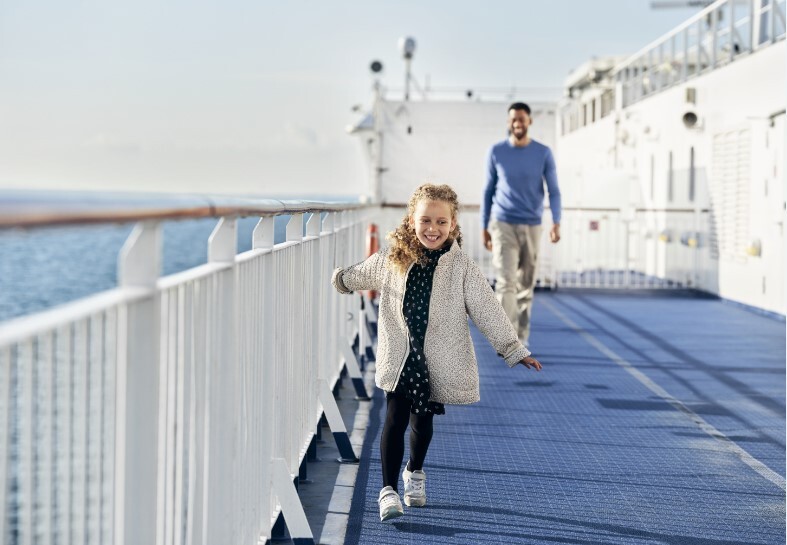 Little girl running and smiling on sun deck on the ferry with her father